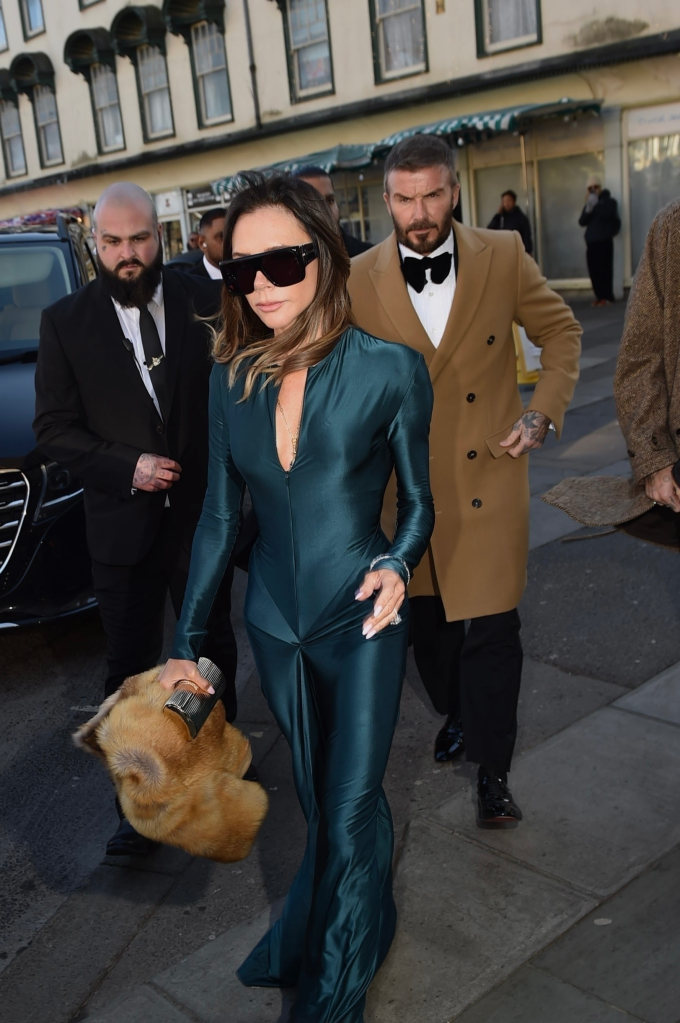 Victoria Beckham in a green satin dress and black sunglasses, with David Beckham in a tan coat and tuxedo.