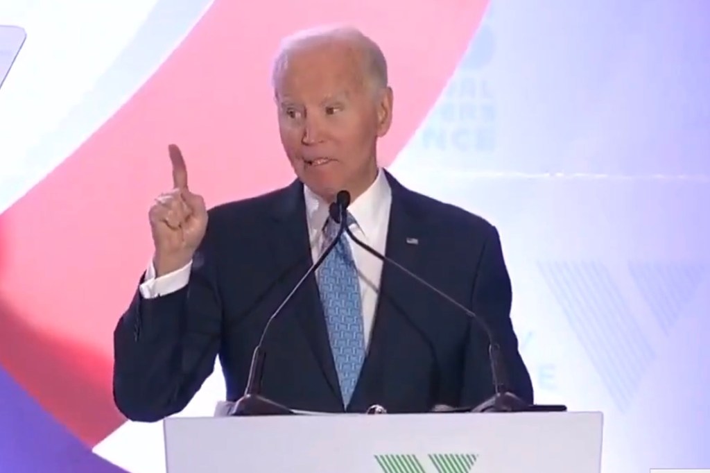 President Biden at a podium, speaking with a microphone, pointing his right index finger upwards.