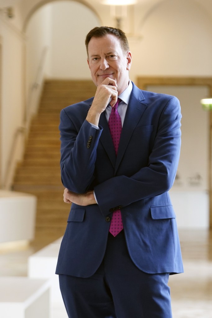 Bill de Blasio in a blue suit and red tie, posing with his hand on his chin.
