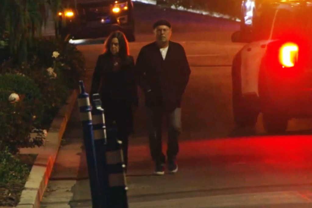 Billy Crystal outside Rob Reiner’s home after two people found dead, with red flashing lights from emergency vehicles in the background.