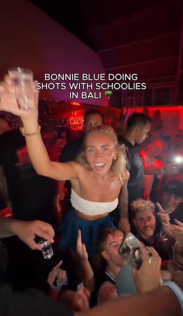 Bonnie Blue partying in a crowded club, holding a shot glass and smiling.