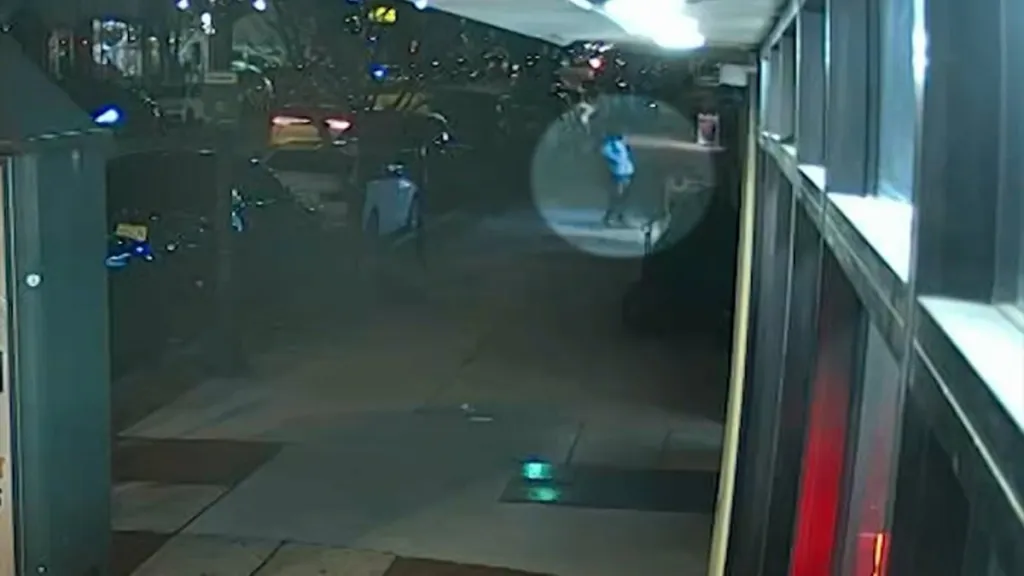 Security camera footage of a street at night with a person in a blue shirt highlighted in a circle.