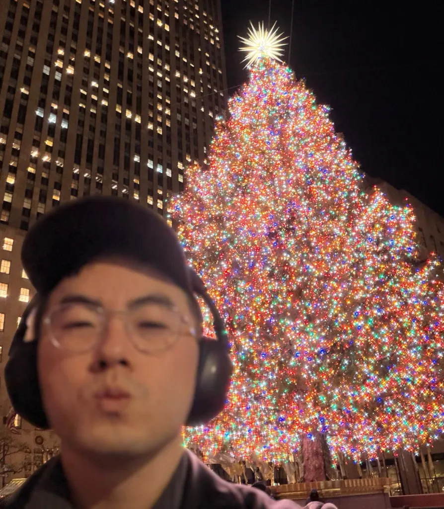 Bowen Yang taking a selfie in front of the Rockefeller Center Christmas tree.