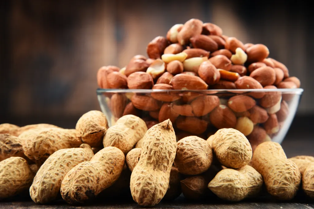 Peanuts in shells and shelled peanuts in a bowl on a wooden table.