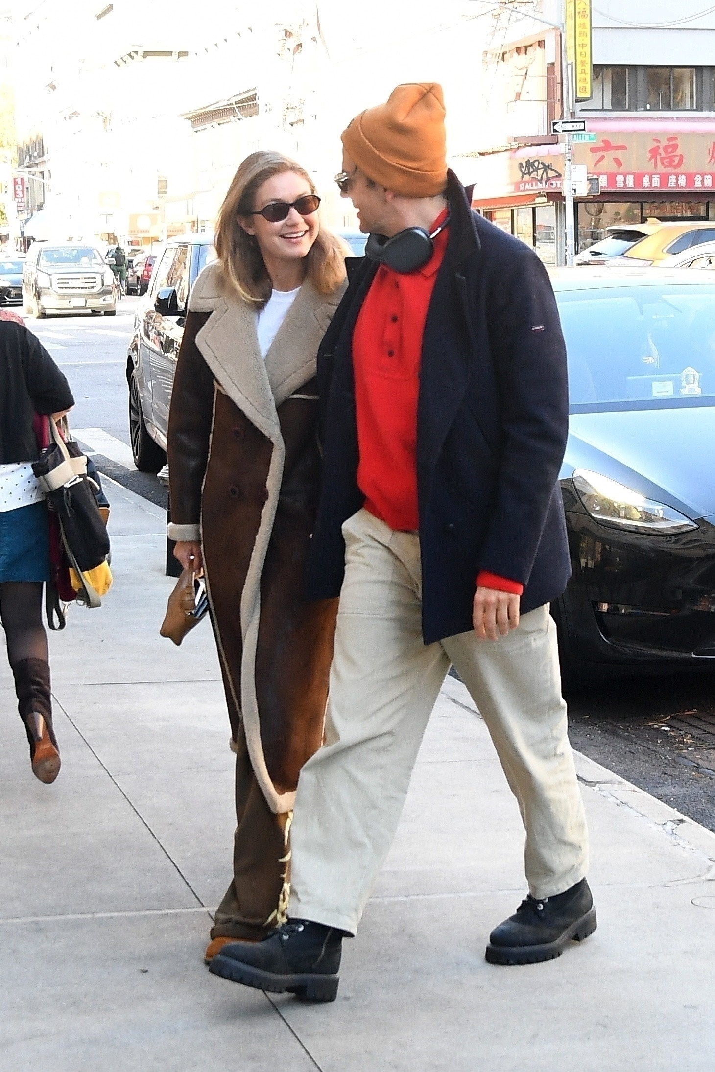 Gigi Hadid and Bradley Cooper walking down a city street, Hadid smiling at Cooper who wears an orange beanie.