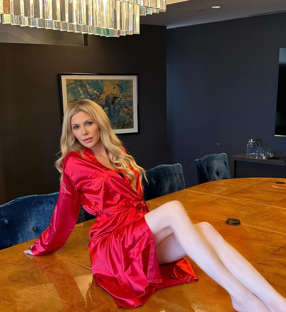 Brandi Glanville posing in a red satin robe on a conference table.