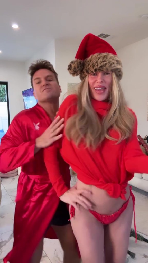 Brandi Glanville wearing a Santa hat and red bikini bottoms with a man in a red robe.