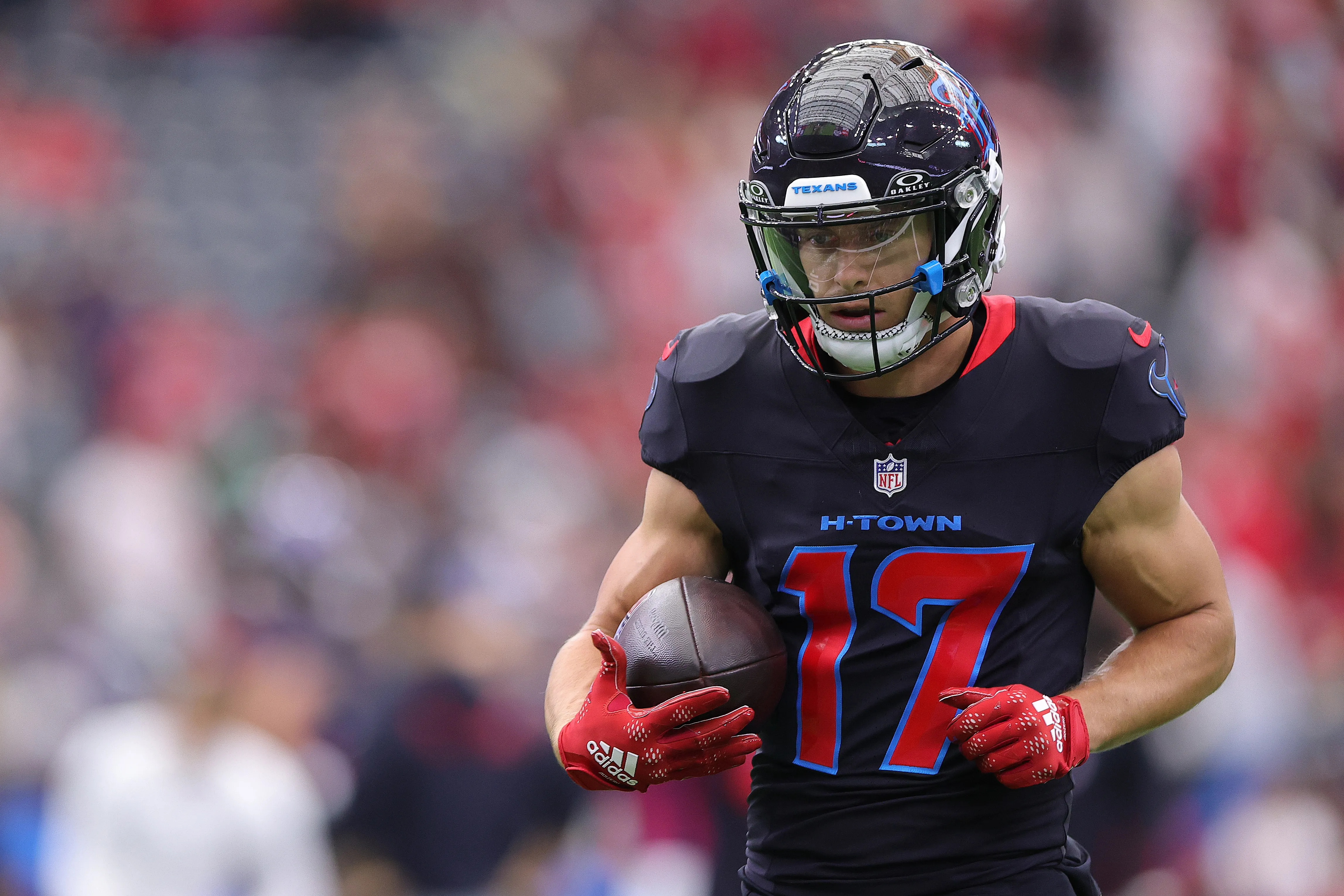 Houston Texans player Braxton Berrios #17 in a dark uniform and red gloves, holding a football.