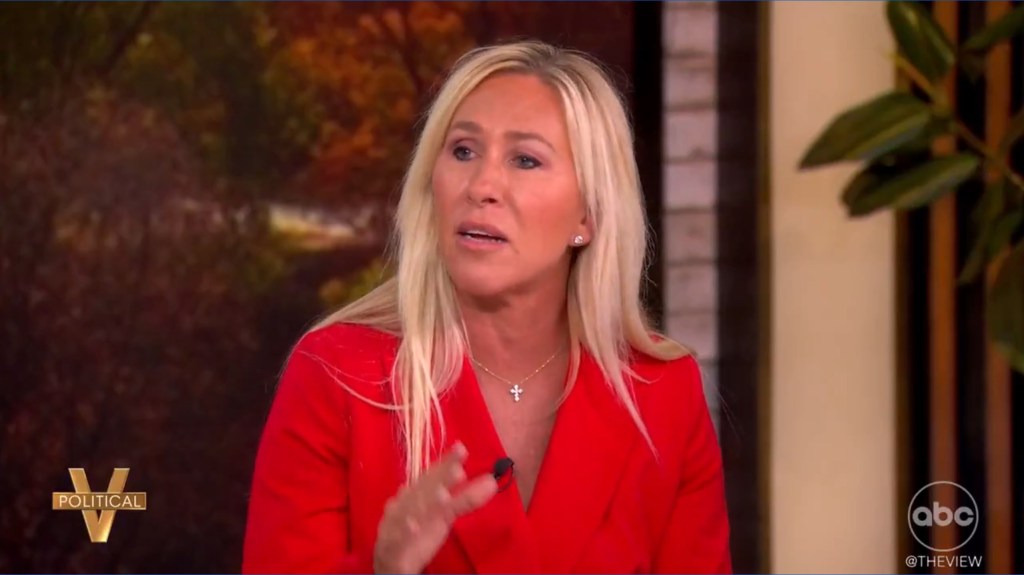 Marjorie Taylor Greene with long blonde hair, wearing a red blazer and a cross necklace, speaks on The View.