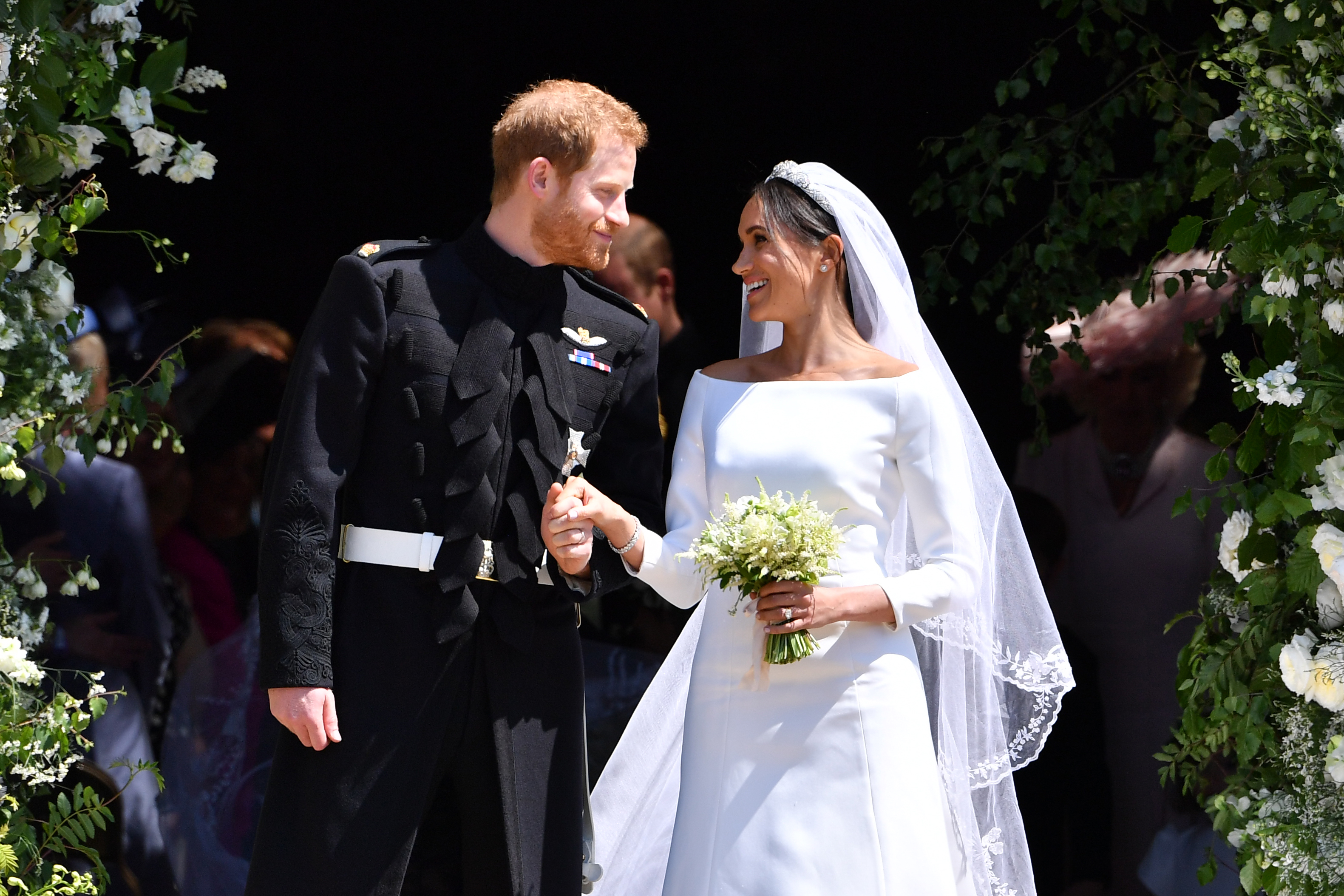 Meghan Markle in a white wedding gown holding hands with Prince Harry in a military uniform.