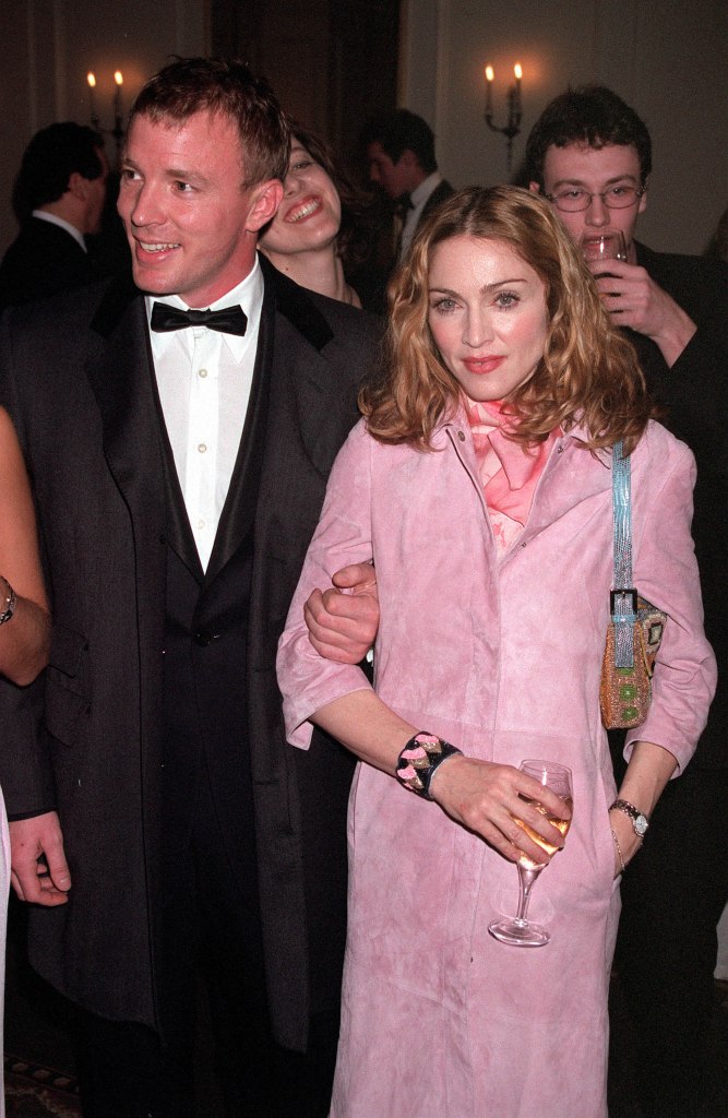 Guy Ritchie in a black suit and Madonna in a pink jacket holding a drink.