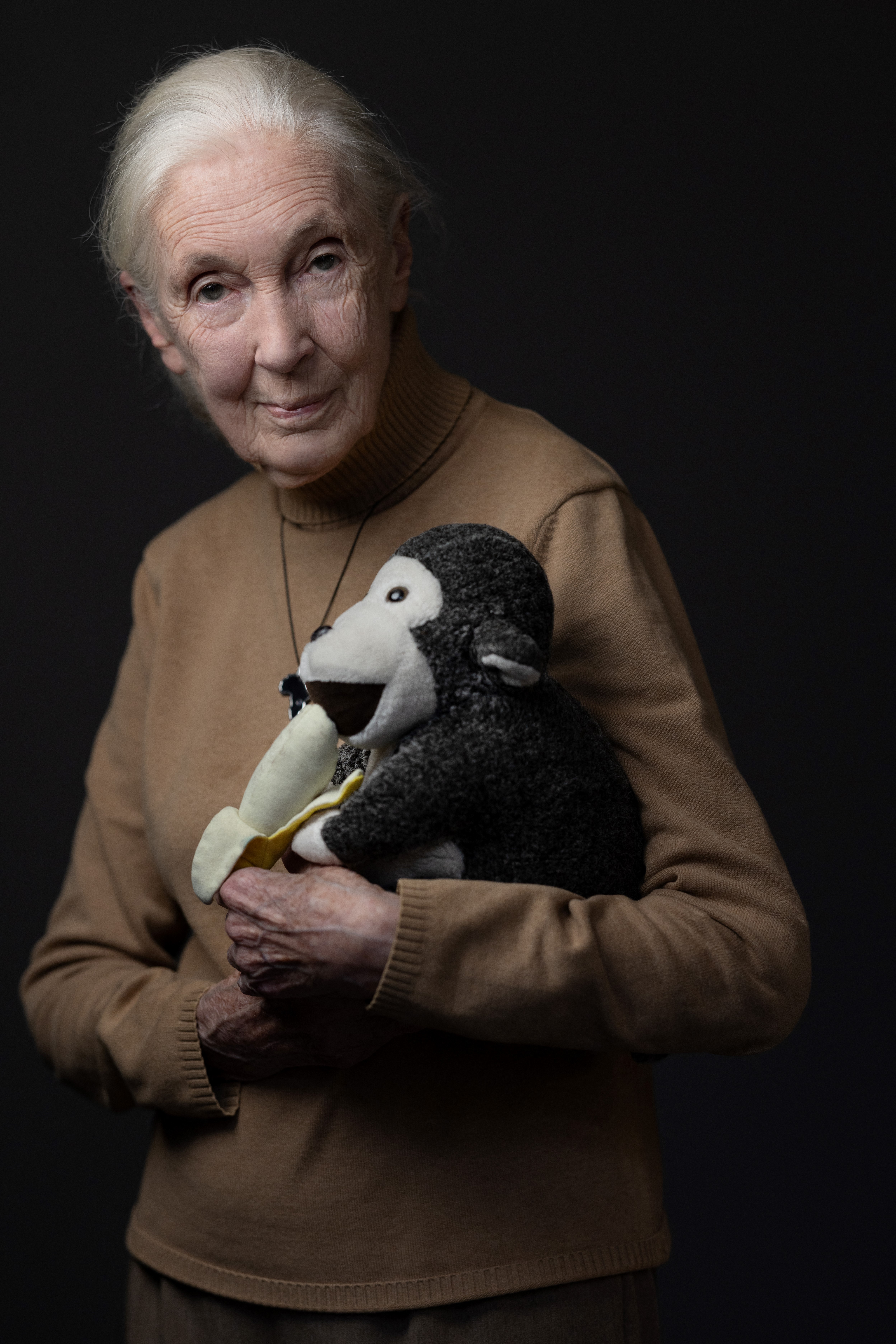 Jane Goodall holds her mascot, a stuffed monkey holding a banana.