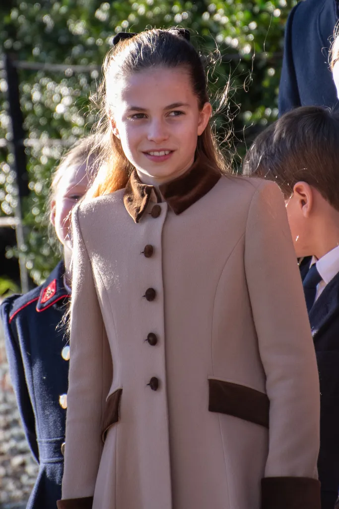 Princess Charlotte in a light beige coat with brown collar and accents, smiling.
