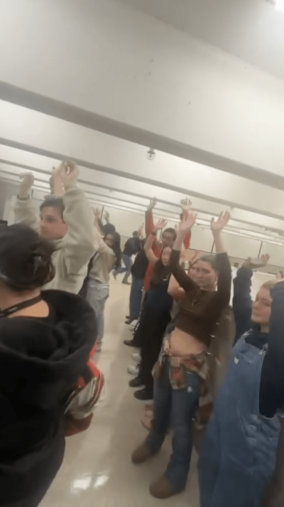 Students hiding from a gunman in a university library with their hands raised.