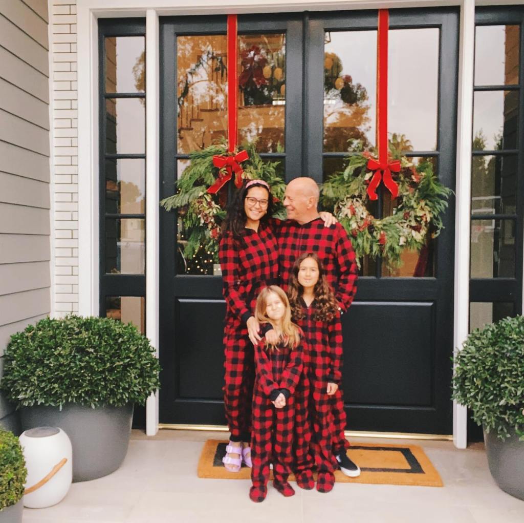 Bruce Willis, Emma, and their two daughters pose in matching red and black plaid pajamas in front of a door decorated with Christmas wreaths.