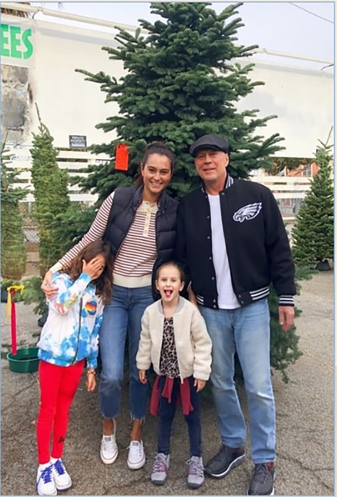 Bruce Willis and his wife, Emma Heming, with their two daughters, standing in front of a Christmas tree.