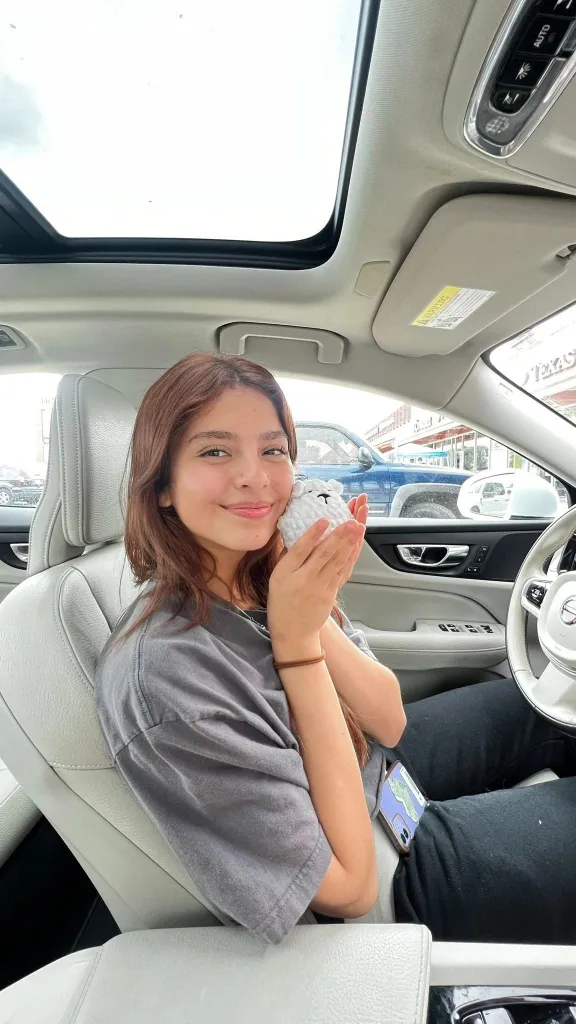 Camila Mendoza Olmos holding a small white knitted sheep toy in a car.
