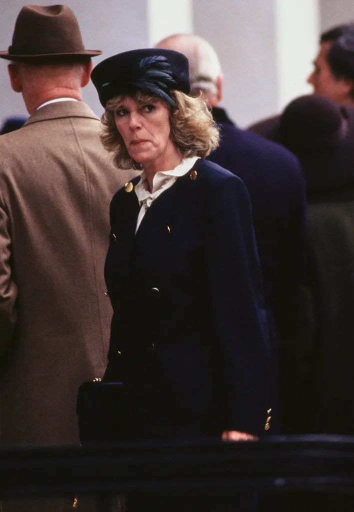 Camilla Parker Bowles in a dark blue coat and matching hat with a feather detail, among a crowd.