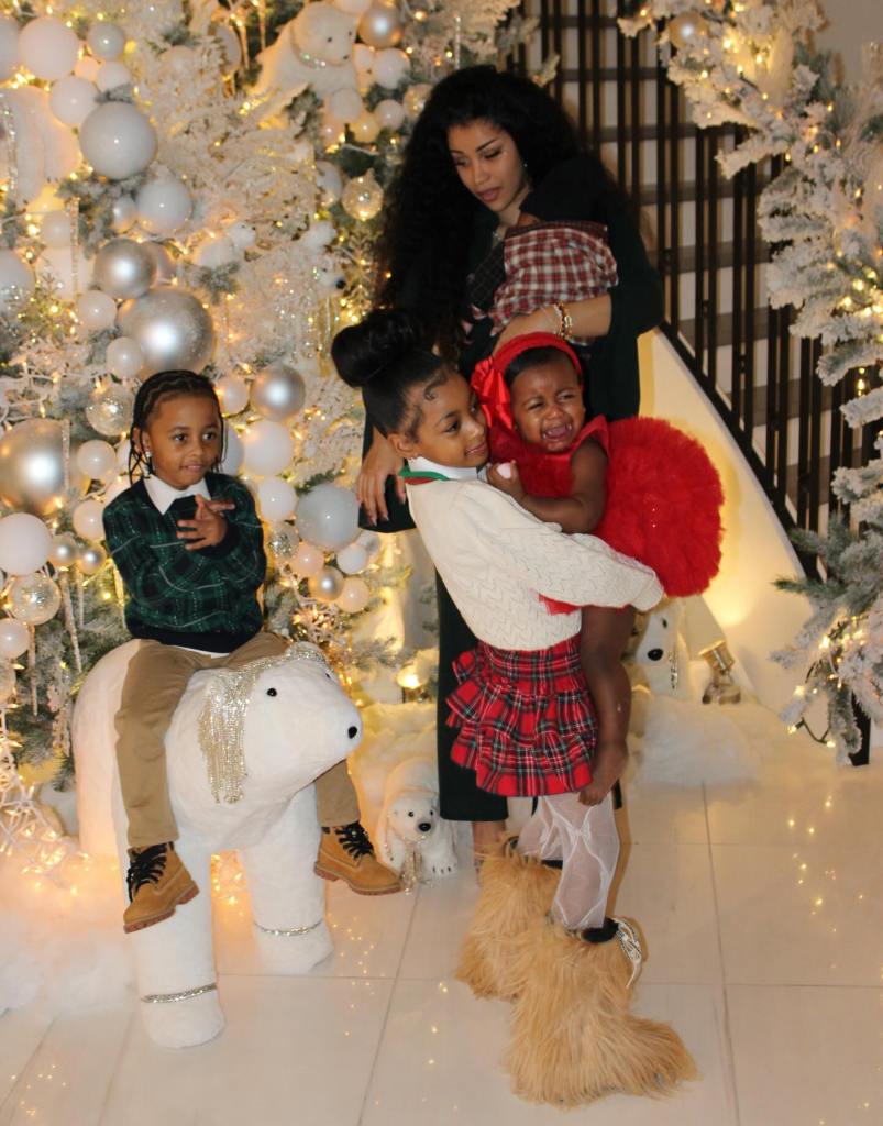 Cardi B holding a baby with two other children in front of a white Christmas tree.