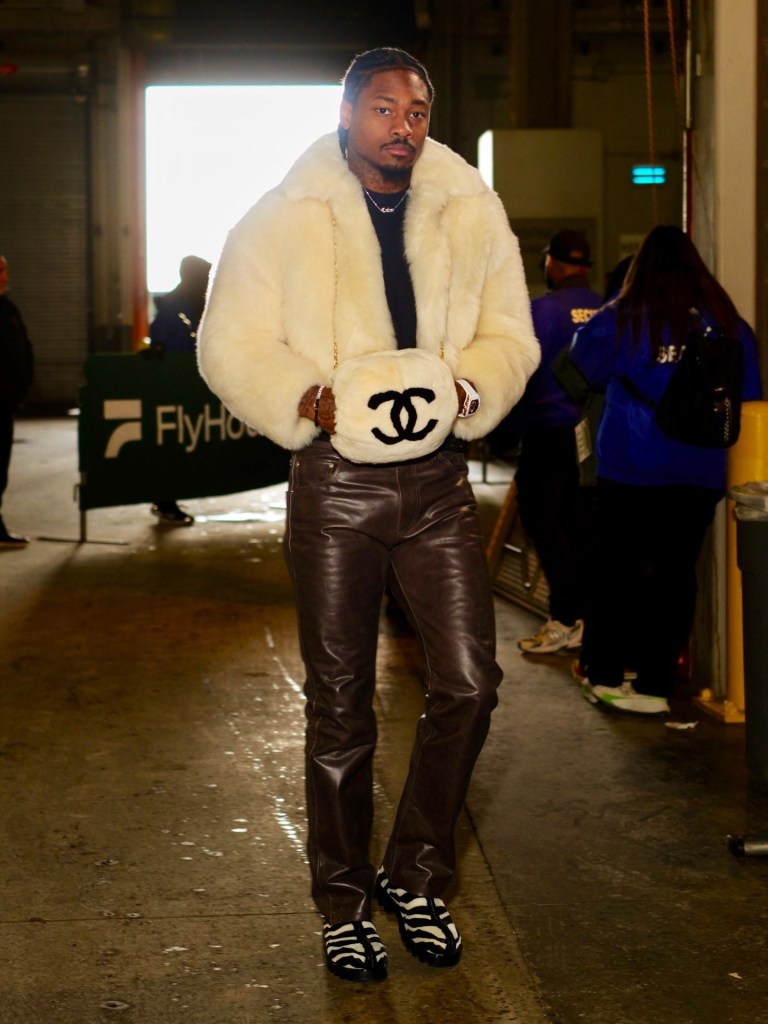Stefon Diggs in a white fur coat, brown leather pants, and a white Chanel handbag.