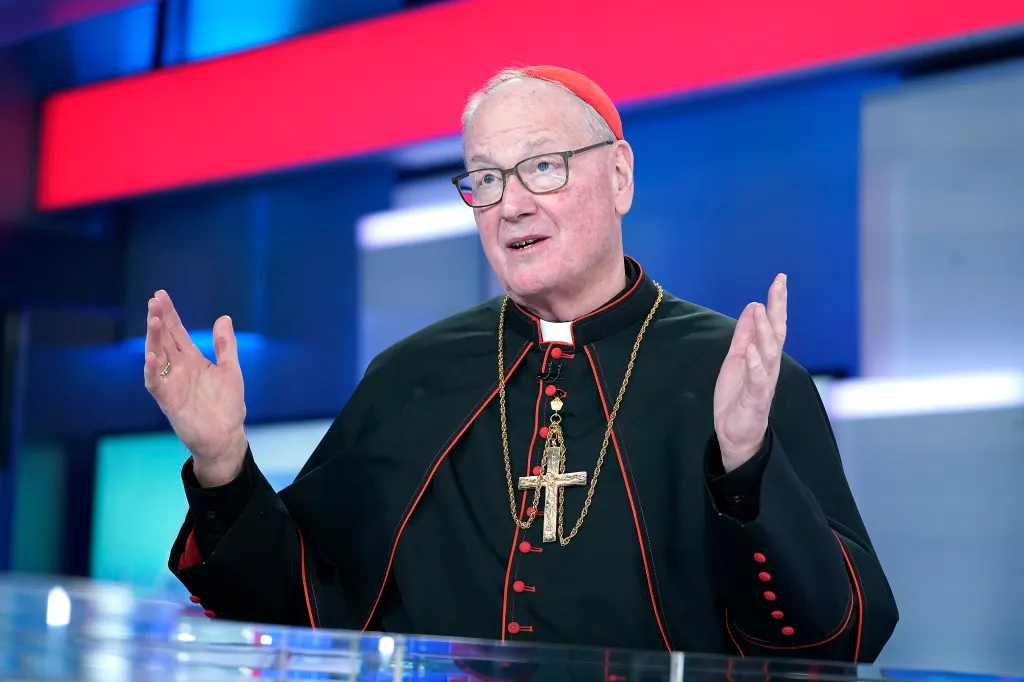 Cardinal Timothy Dolan speaking at a studio with his hands raised.