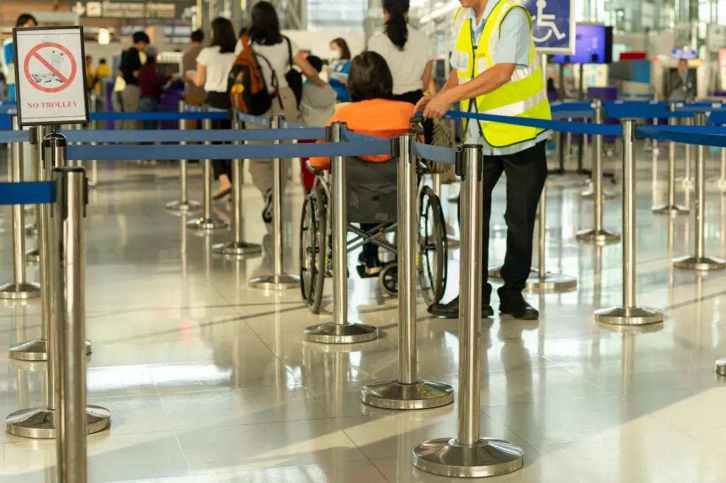 A caretaker pushing a senior woman in a wheelchair at an airport check-in line.