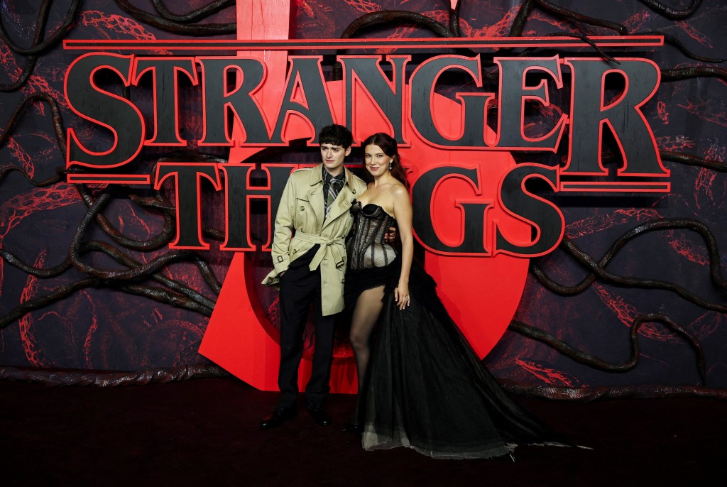 Noah Schnapp and Millie Bobby Brown pose in front of a 