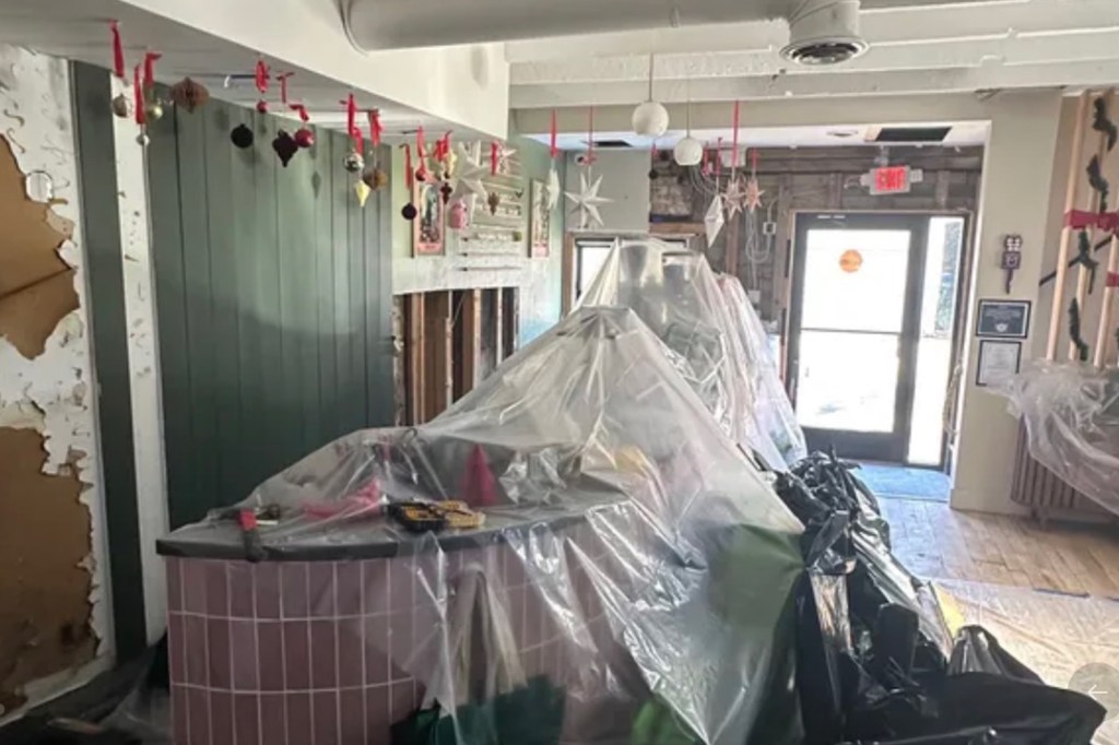 Interior of a space undergoing renovation with furniture covered in plastic and exposed walls.