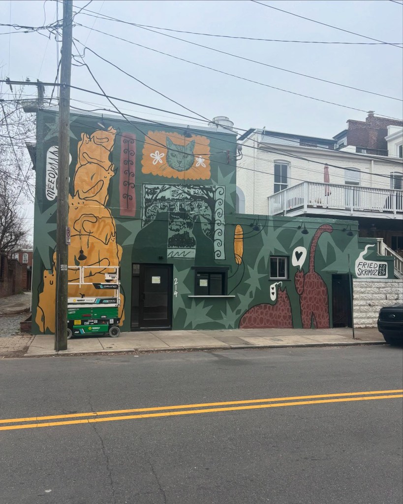 Mural on the side of a building with multiple cats and the words