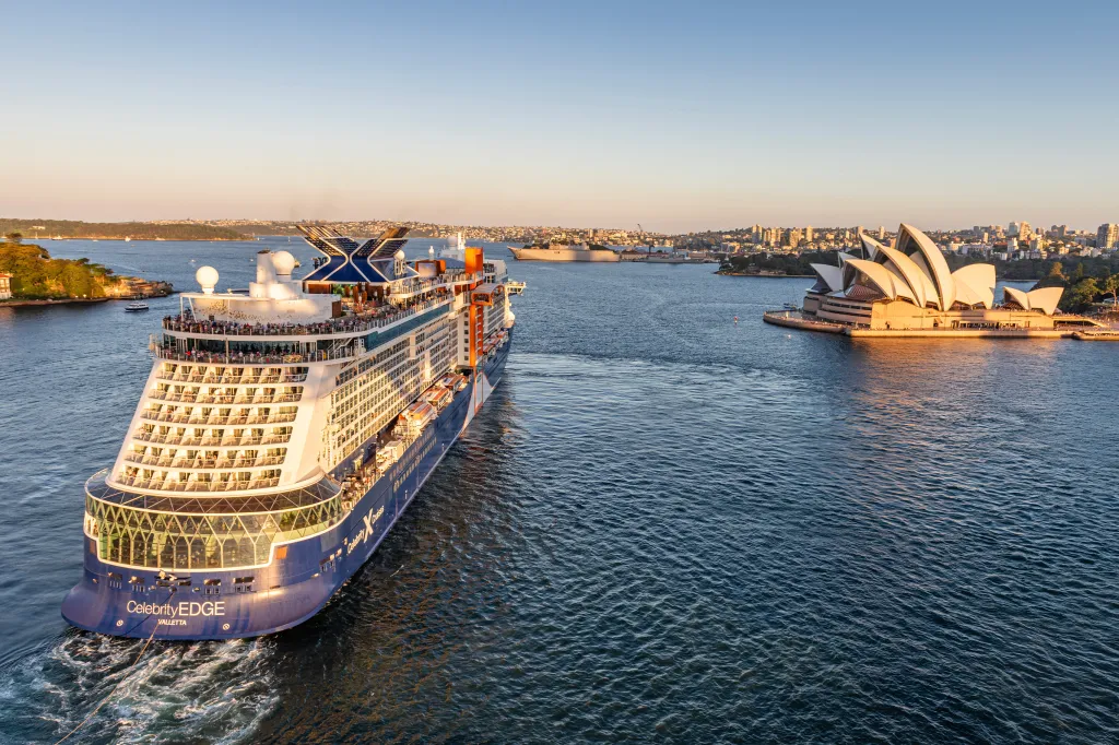 A Celebrity Edge cruise ship sailing in front of the Sydney Opera House at sunset.