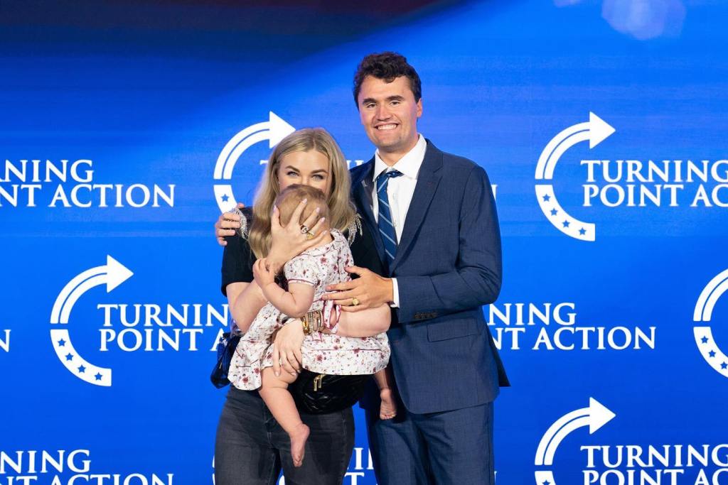 Erika Kirk holding a baby next to Charlie Kirk, with
