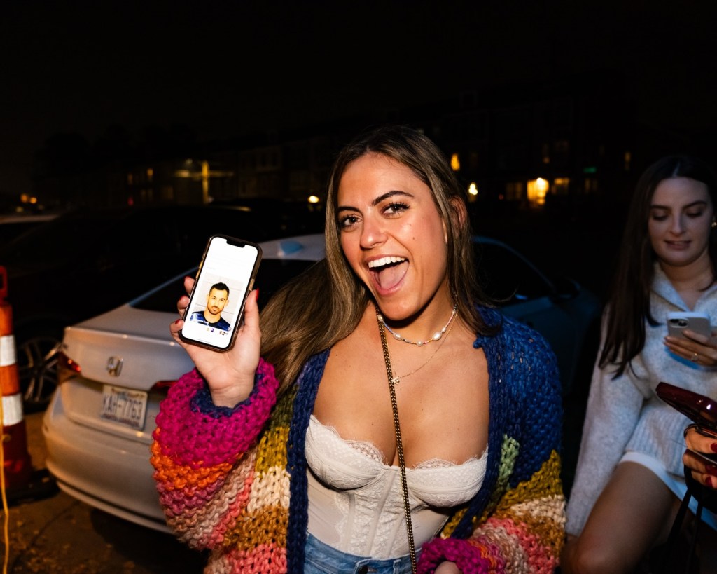 A woman holding up a phone displaying a picture of a man's face.