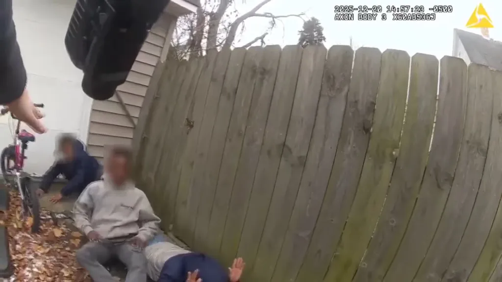 Bodycam footage showing a person holding out a hand towards three blurred individuals on the ground by a wooden fence.