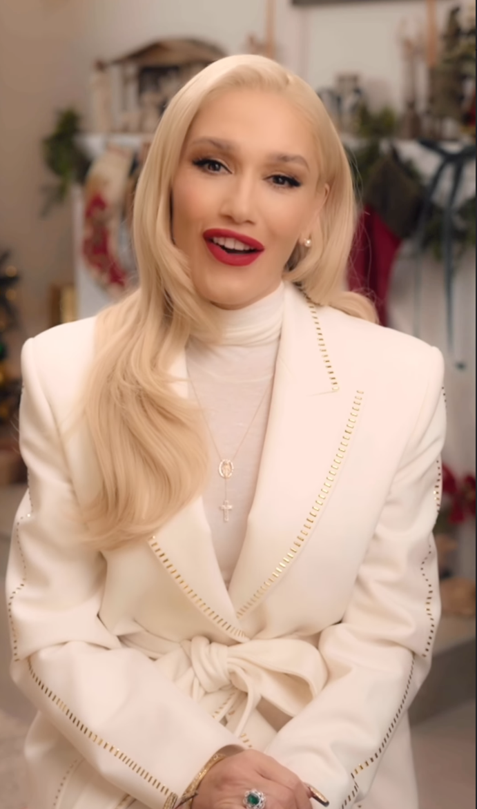 Gwen Stefani in a white blazer and white turtleneck, with a rosary necklace.