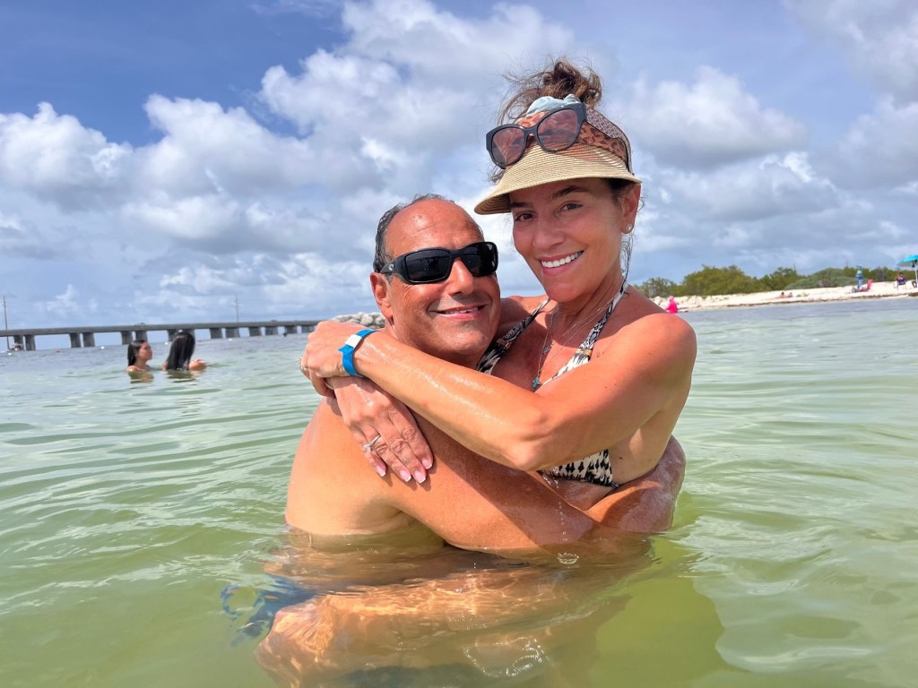 A man in sunglasses holding a woman in a bikini and visor in the water.