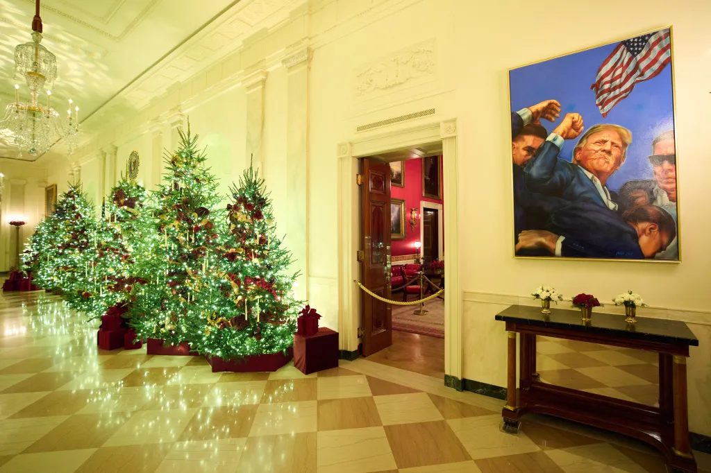 Christmas trees decorating the Cross Hall of the White House, with a painting of Donald Trump.