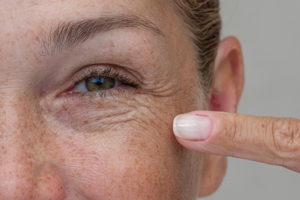 Close-up of a middle-aged woman laughing and pointing at crow's feet by her eye.