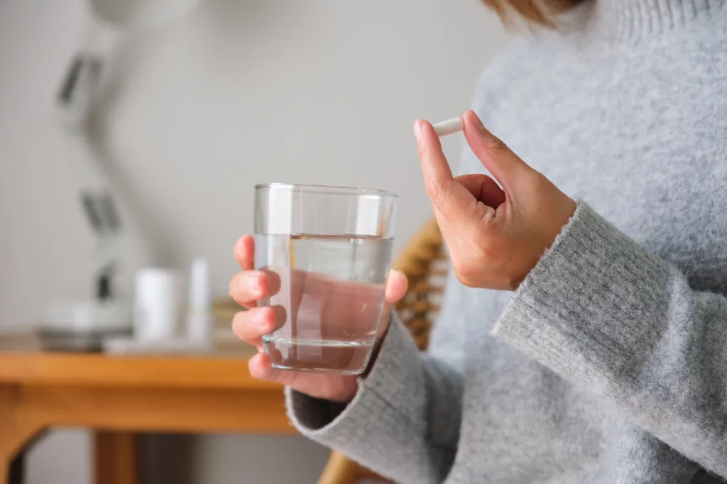 A woman holding a white pill and a glass of water.