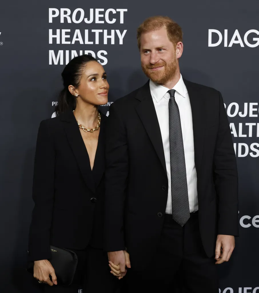 Meghan Markle and Prince Harry holding hands and looking at each other on a red carpet.