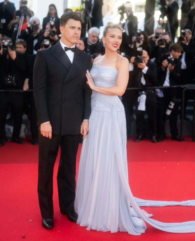 Colin Jost in a black tuxedo and Scarlett Johansson in a strapless light blue gown on a red carpet.