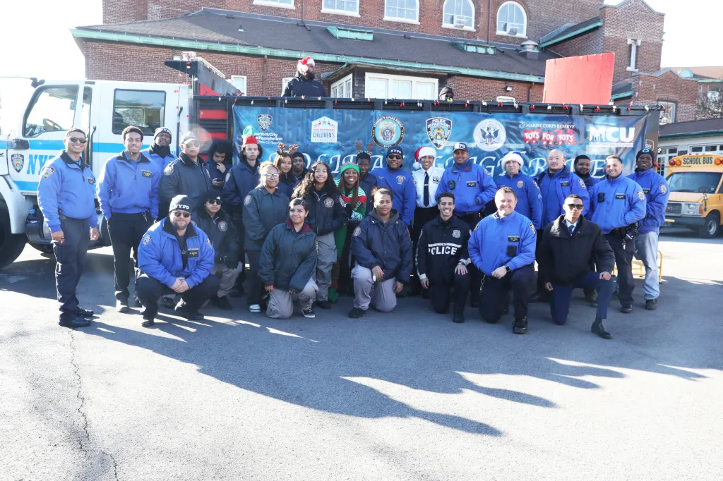A group of police officers and children posing for a photo in front of a truck, at the St. Joseph’s School for the Deaf, for a police foundation sleigh ride and toys giveaway.