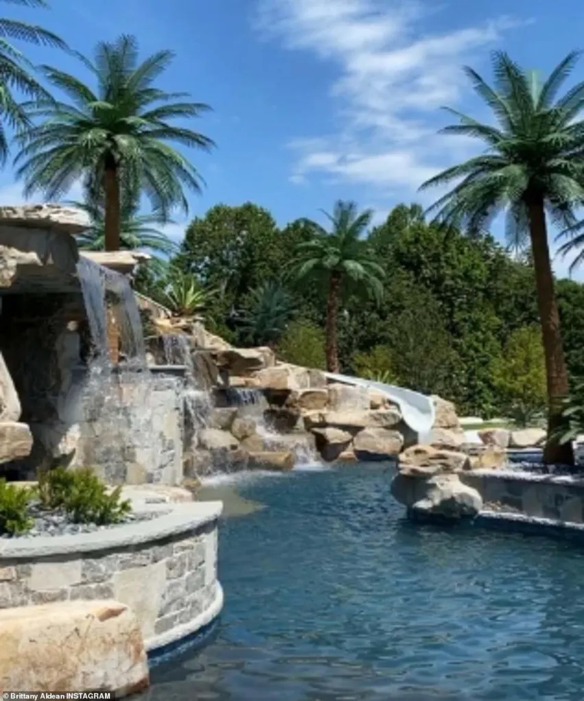 A swimming pool with rock waterfalls, a white slide, and palm trees surrounding it.