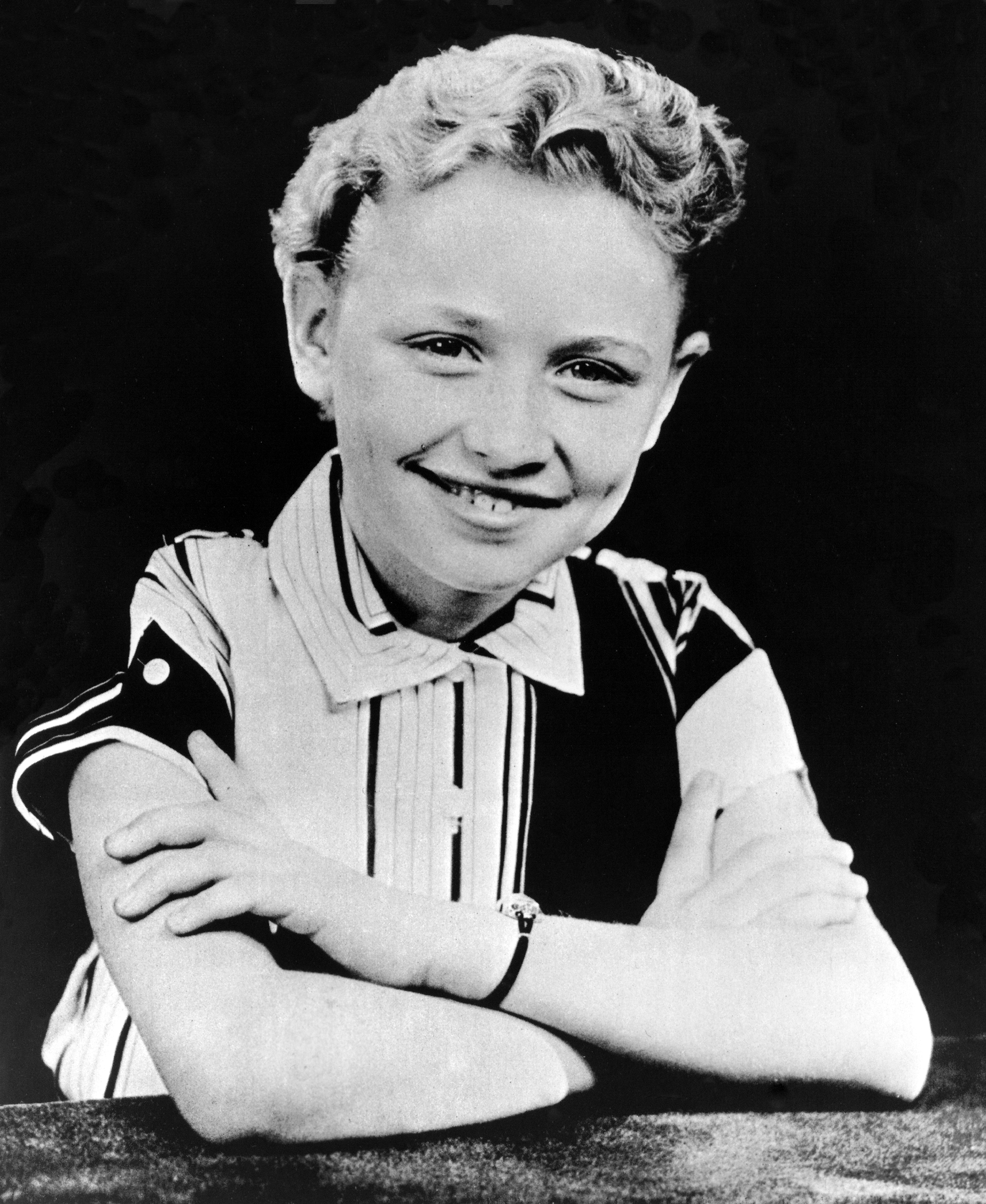 Young Dolly Parton smiling with her arms crossed.