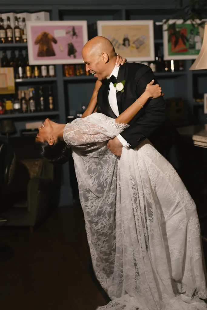 A happy bride in a white lace dress dips while dancing with her groom in a black tuxedo.