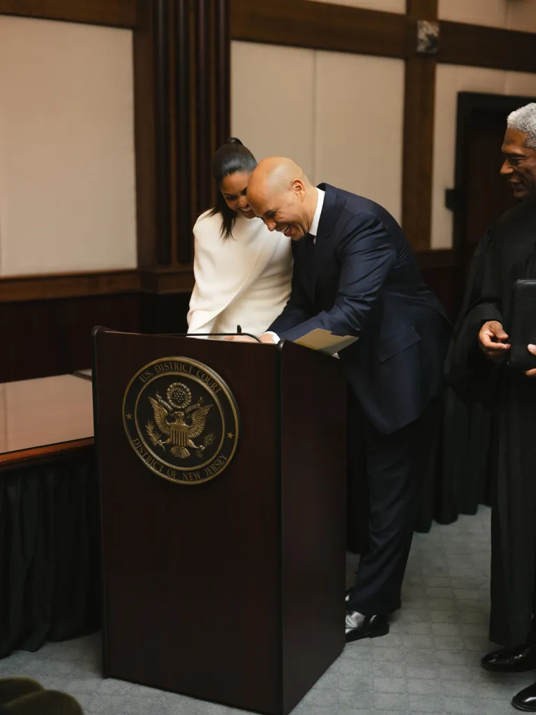 Cory Booker signs documents next to Alexis Lewis and a judge at a courthouse.
