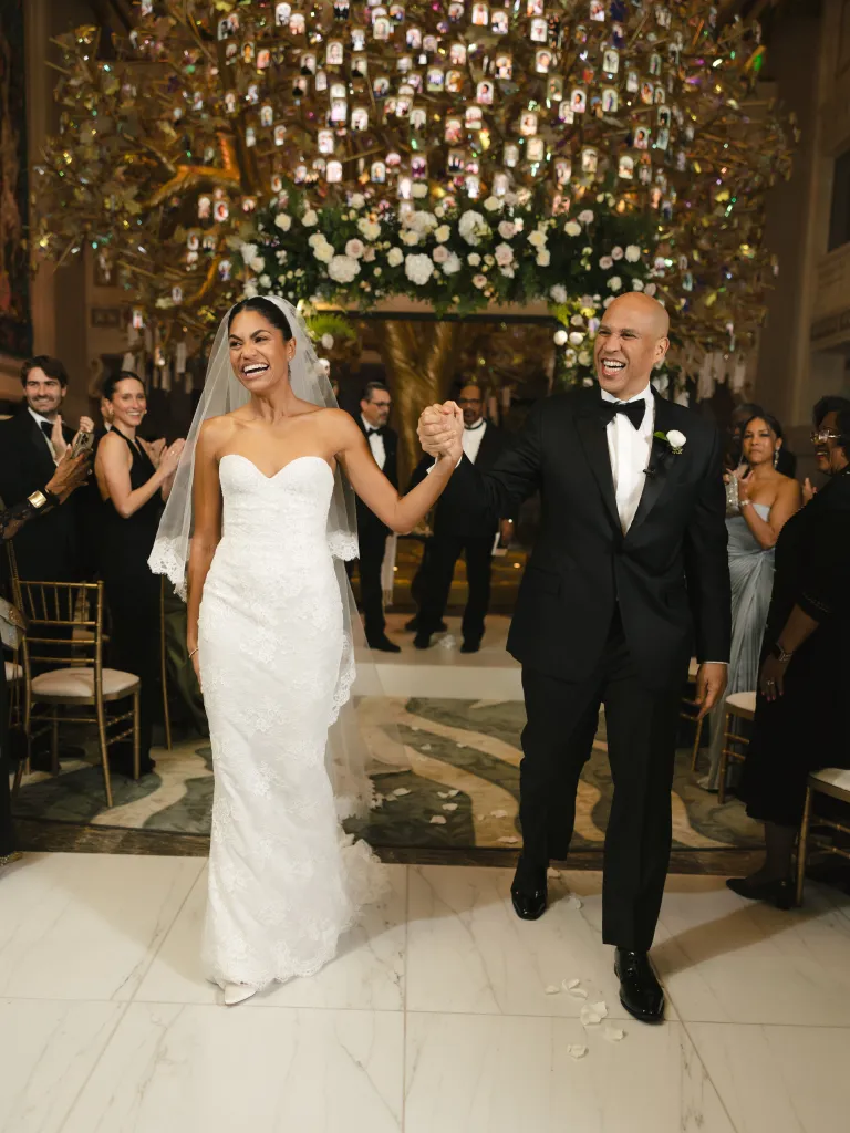 Cory Booker and Alexis Lewis walk down the aisle holding hands, smiling and laughing, after their wedding ceremony.