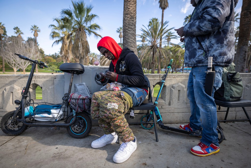Two men hanging out at MacArthur Park, one seated and looking at headphones, the other standing.