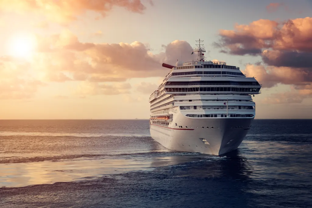 A large white cruise ship sailing in the ocean at sunset.