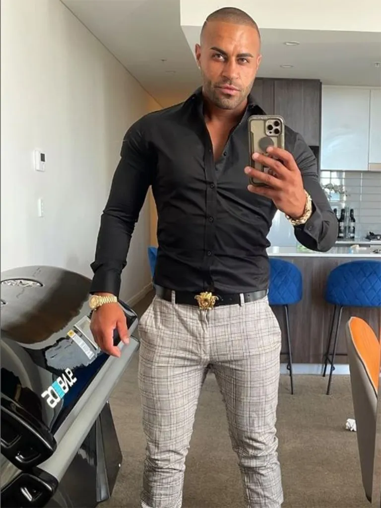 Danny Zayat, the man accused of murdering his former partner, poses for a mirror selfie in a black button-down shirt and plaid pants.