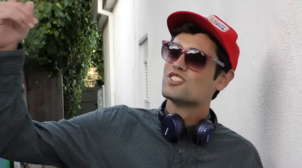 Nick Reiner in a red cap and sunglasses, gesturing.